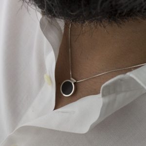 Colgante de plata 925 con incrustación de madera de ébano. Diámetro 15mm, grosor 4mm. Cadena de plata 925, longitud opcional 40cm, 45cm, o 50cm. Cierre de "reasa" sencillo. Objeto diseñado y fabricado artesanalmente en Madrid, España, por el estudio-taller de malicia. Este colgante ha sido fabricado por personas que disfrutan su trabajo.