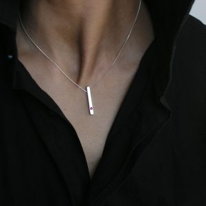 Colgante de plata 925 mate de 25mm de longitud, con rubí talla brillante de 2mm.  Cadena de plata 925, longitud opcional 40, 45 o 50cm. Cierre de "reasa" pequeña. Objeto diseñado y fabricado artesanalmente en Madrid, España, por el estudio-taller de malicia. Este anillo ha sido fabricado por personas que disfrutan su trabajo.