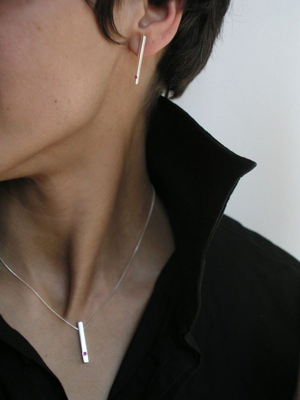 Colgante de plata 925 mate de 25mm de longitud, con rubí talla brillante de 2mm.  Cadena de plata 925, longitud opcional 40, 45 o 50cm. Cierre de "reasa" pequeña. Objeto diseñado y fabricado artesanalmente en Madrid, España, por el estudio-taller de malicia. Este anillo ha sido fabricado por personas que disfrutan su trabajo.