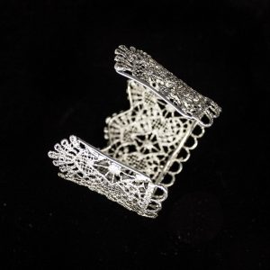 Pieza única diseñada y fabricada artesanalmente por el estudio-taller de malicia. Plata 925 envejecida. Objeto fabricado por personas que disfrutan su trabajo. En 2016, con motivo 400 aniversario del fallecimiento de Miguel de Cervantes y Saavedra, el estudio-taller edita una serie de piezas de joyería inspiradas en la figura del literato, la estética de su tiempo, y su obra más universal, El Quijote. Esta pieza construida íntegramente con plata 925, recrea aquellas puñetas bordadas que asomaban bajo las mangas del sobrio atuendo negro del típico hidalgo español del Renacimiento y Barroco. Esta estética en el vestir fue inmortalizada por el Greco en su “caballero de la mano en el pecho”, otrora considerado erróneamente un retrato de Cervantes.