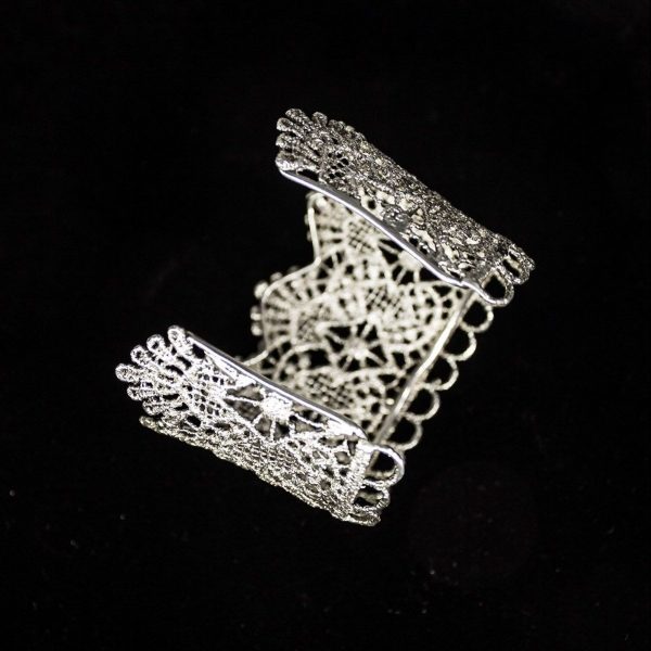 Pieza única diseñada y fabricada artesanalmente por el estudio-taller de malicia. Plata 925 envejecida. Objeto fabricado por personas que disfrutan su trabajo. En 2016, con motivo 400 aniversario del fallecimiento de Miguel de Cervantes y Saavedra, el estudio-taller edita una serie de piezas de joyería inspiradas en la figura del literato, la estética de su tiempo, y su obra más universal, El Quijote. Esta pieza construida íntegramente con plata 925, recrea aquellas puñetas bordadas que asomaban bajo las mangas del sobrio atuendo negro del típico hidalgo español del Renacimiento y Barroco. Esta estética en el vestir fue inmortalizada por el Greco en su “caballero de la mano en el pecho”, otrora considerado erróneamente un retrato de Cervantes.